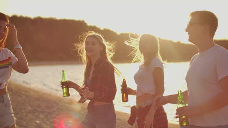Three-hot-girls-are-dancing-in-short-t-shirts-and-shorts-with-beer-on-the-sand-beach-at-sunset.